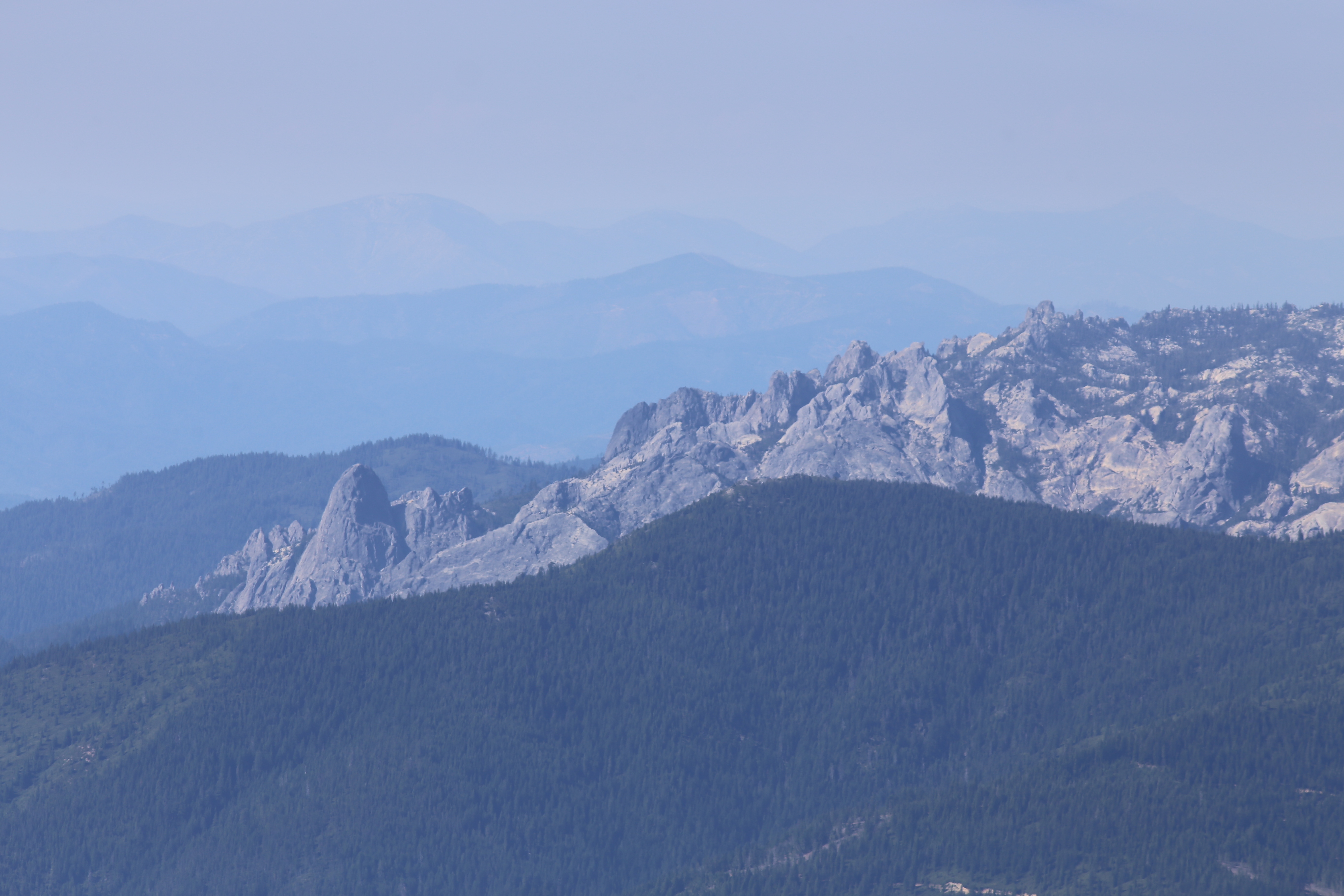 Hazy layered view of jagged granite ridgelines and forested slopes fading into the blue distance